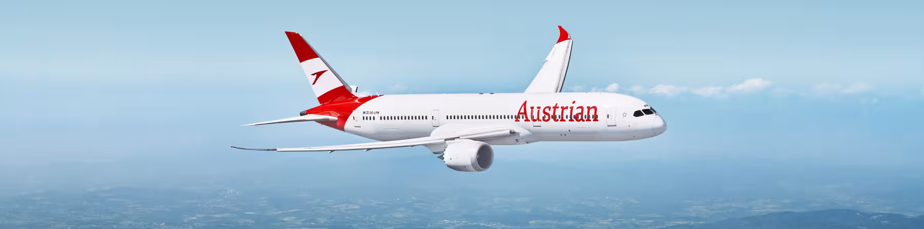Austrian Airlines passenger aircraft in flight against a clear blue sky, viewed side-on, with red tail and engine accents above a green patchwork landscape below.