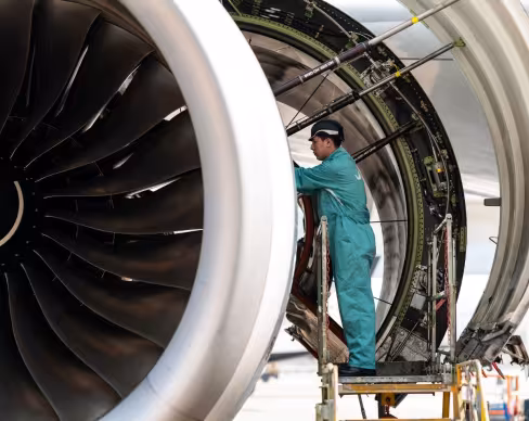 Aircraft engine maintenance technician inspecting a jet engine on a maintenance platform.