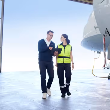 two people walking in a hangar with a tablet