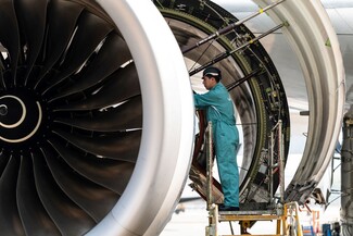 Aircraft engine maintenance technician inspecting a jet engine on a maintenance platform.